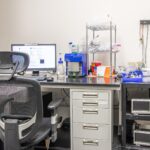 Lab desk with computer monitor, and shelves of scientific tools and supplies.