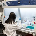 Researcher working under fume hood with lab tools, pipettes, and equipment.